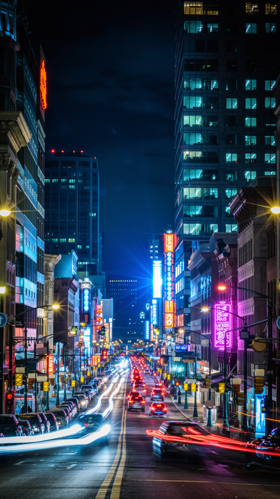 City street in the USA at night with neon lights and cars passing by.